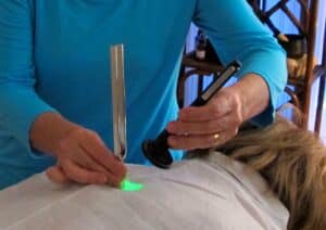 Person holding a light pen and tuning fork to a person's back.