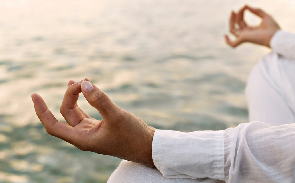 person meditating near water wearing a white linen shirt.