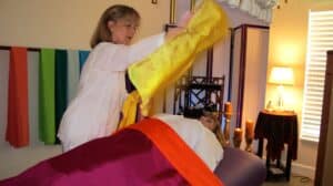 lady draping a yellow scarf over another person laying down meditation session.